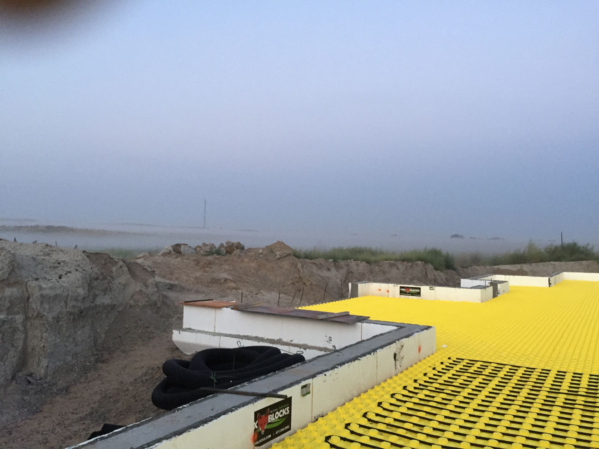 Yellow rooftop under construction beside a foggy coastline, with insulation panels and debris in the foreground