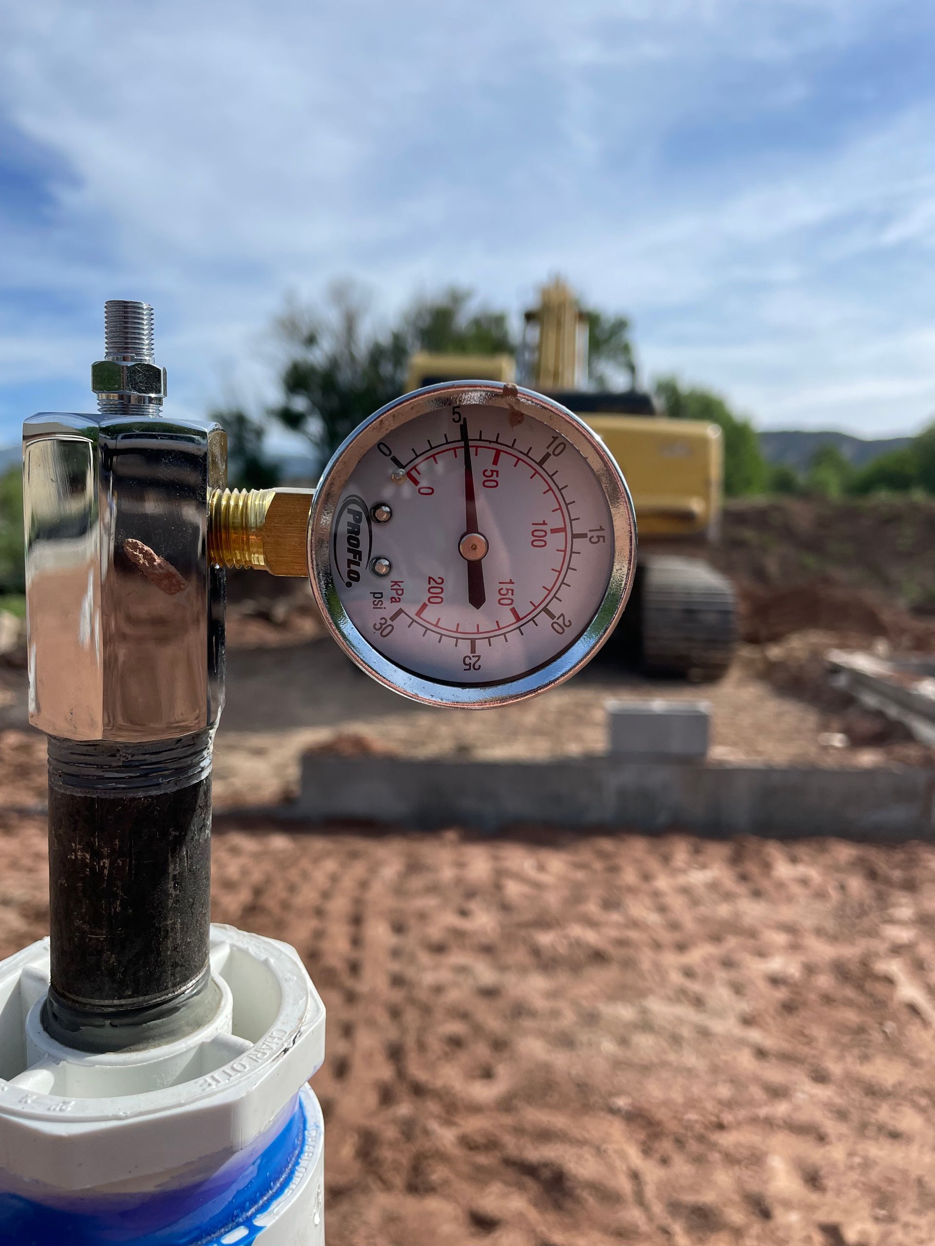 Pressure gauge on a pipe outdoors, with construction equipment blurred in the background.