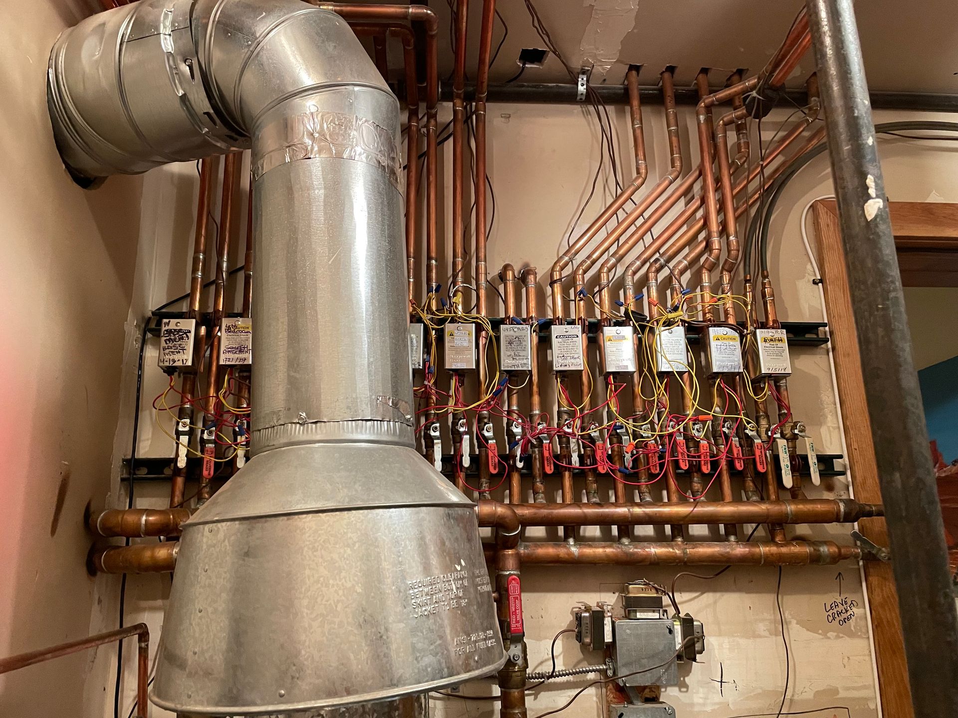 Industrial utility room with large silver ductwork, copper piping, and rows of valves on a wall panel
