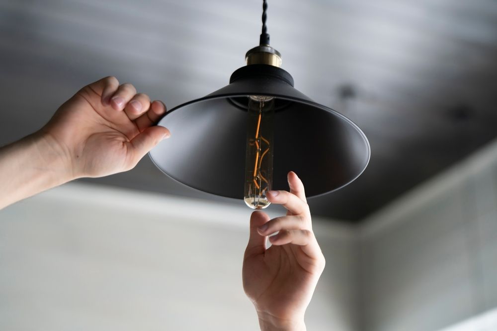 Hands replacing a light bulb in a black ceiling lamp