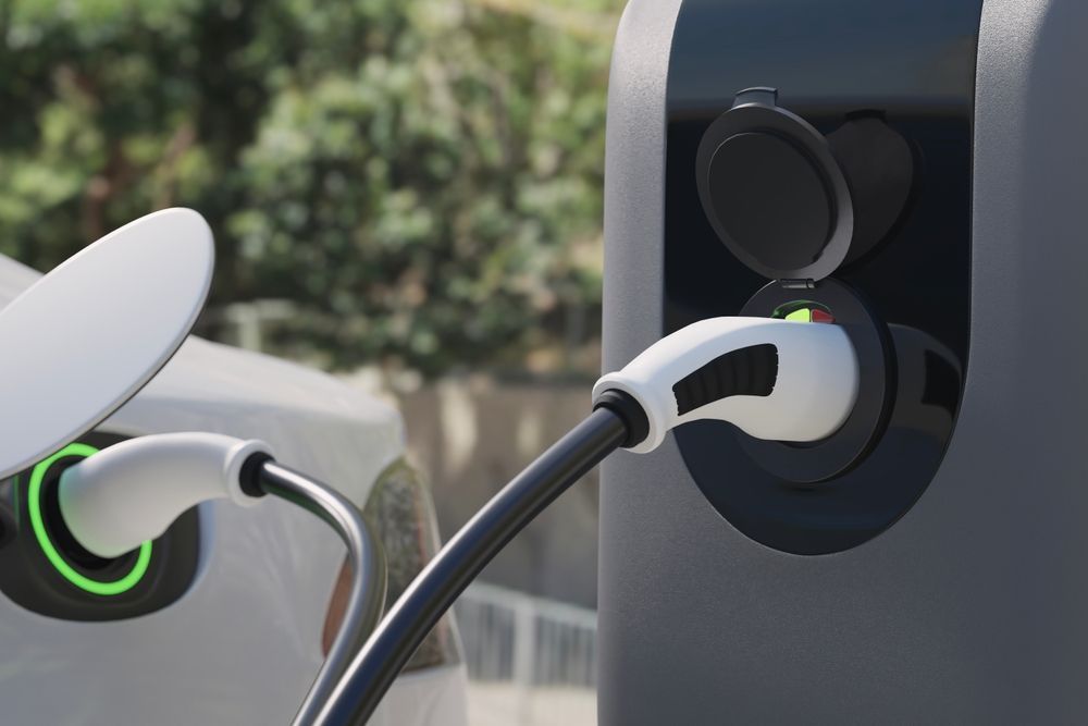 Electric vehicle charging cable plugged into a station, with green indicator lights.