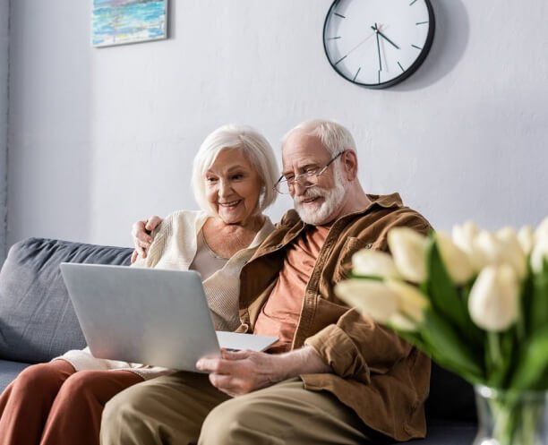 couple sitting on couch browsing laptop