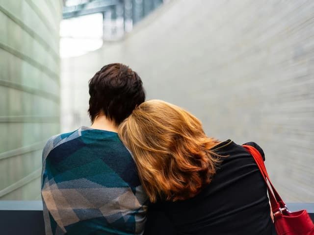 two people sitting down and leaning their heads together