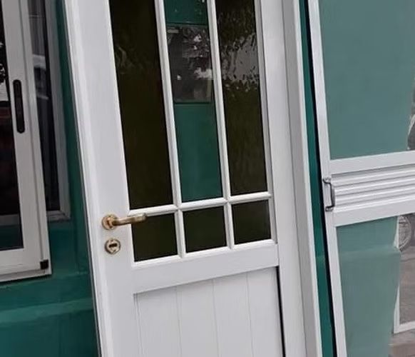 Trabajador midiendo un marco de ventana blanco dentro de una habitación parcialmente renovada.