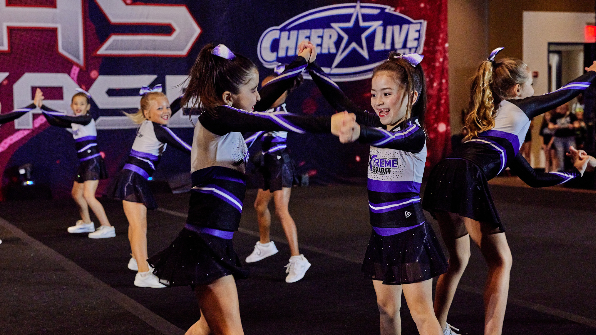 Two young girls are cheering with pom poms in a gym.