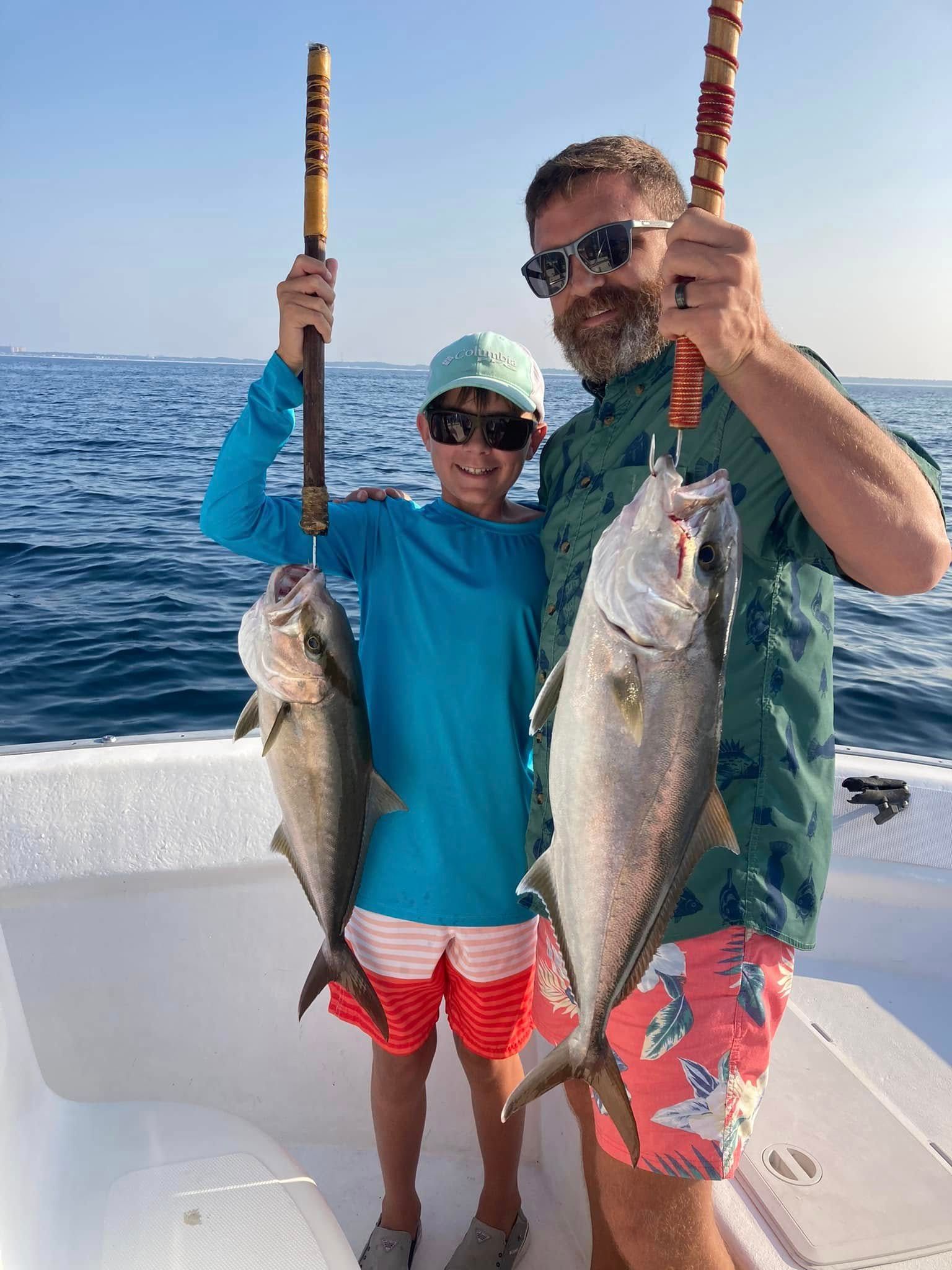 Two people on a boat holding large fish, wearing sunglasses and bright fishing clothes on a sunny ocean trip