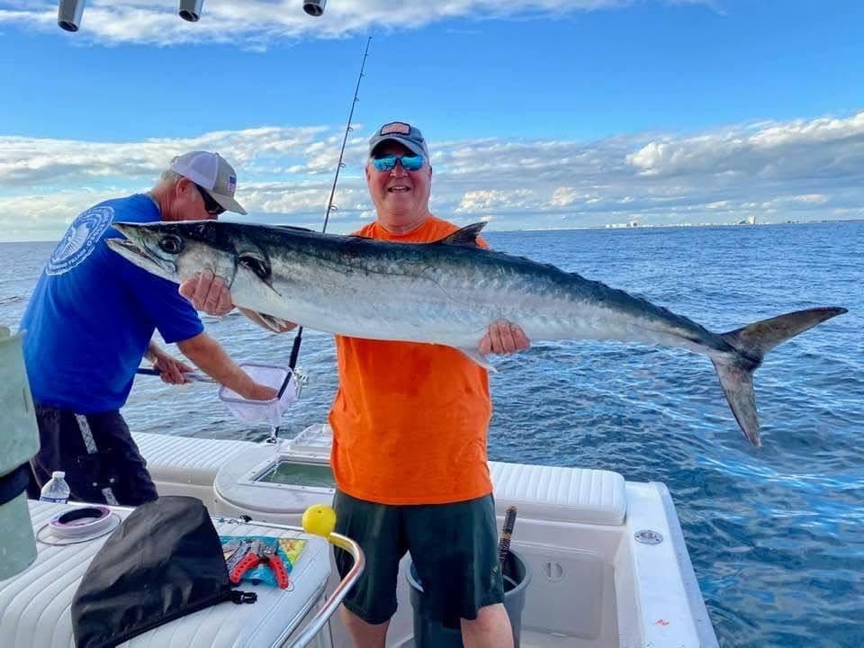 Two people on a boat holding a large fish over the ocean under a partly cloudy sky