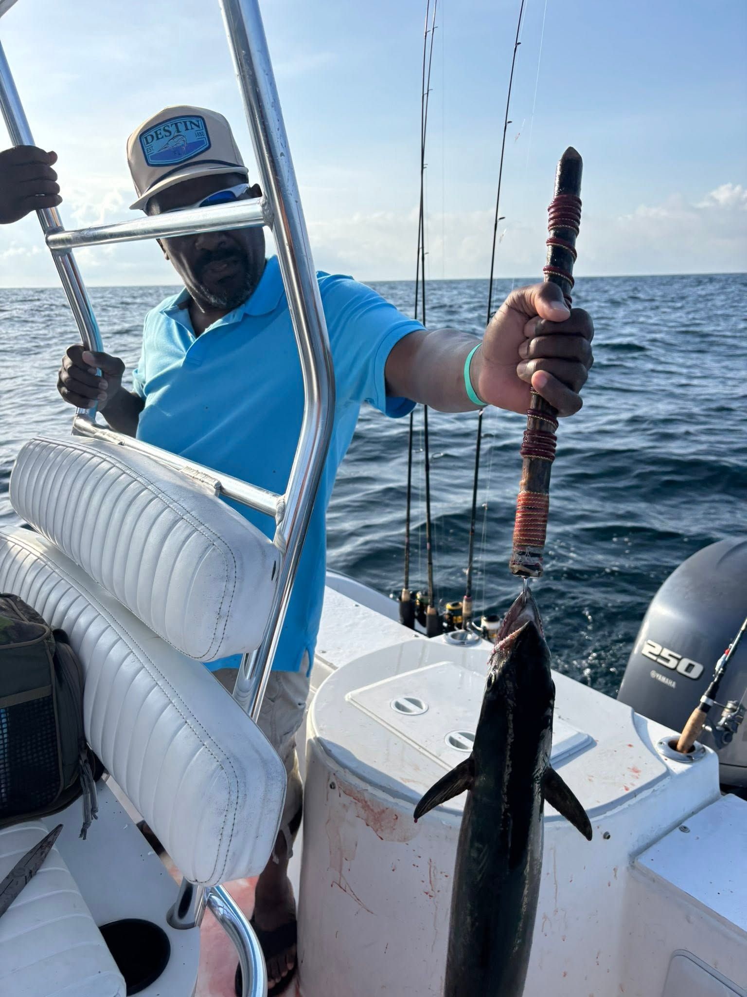 Man on a boat holding fishing rods and a large fish beside the stern on open water.