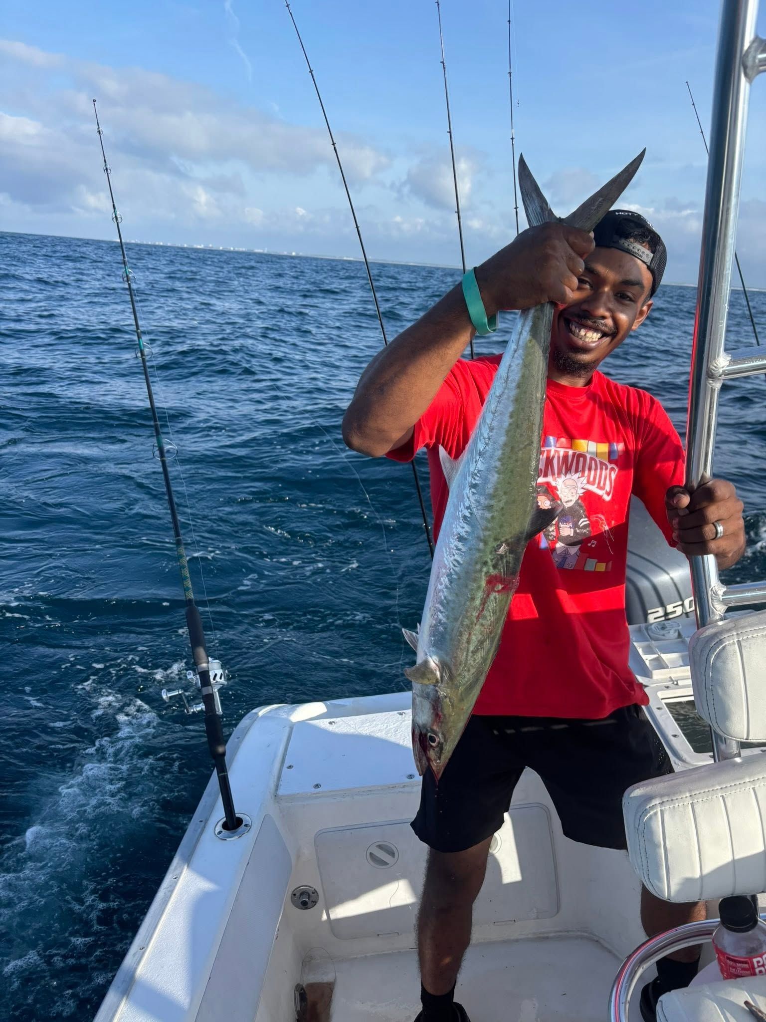 Smiling person on a boat holding a large fish over the ocean, with fishing rods in the background