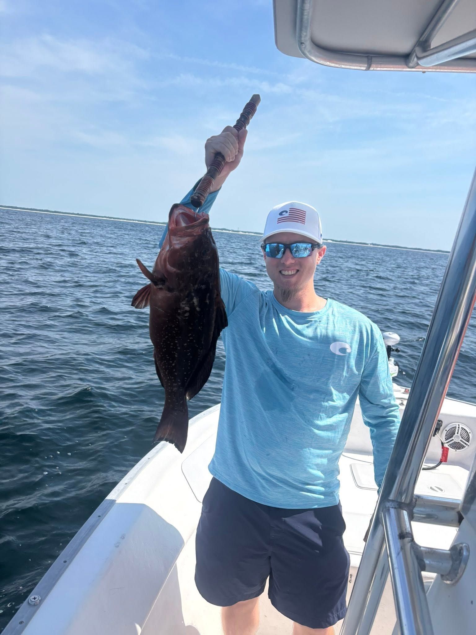 Person on a boat holding up a large fish on a sunny day at sea