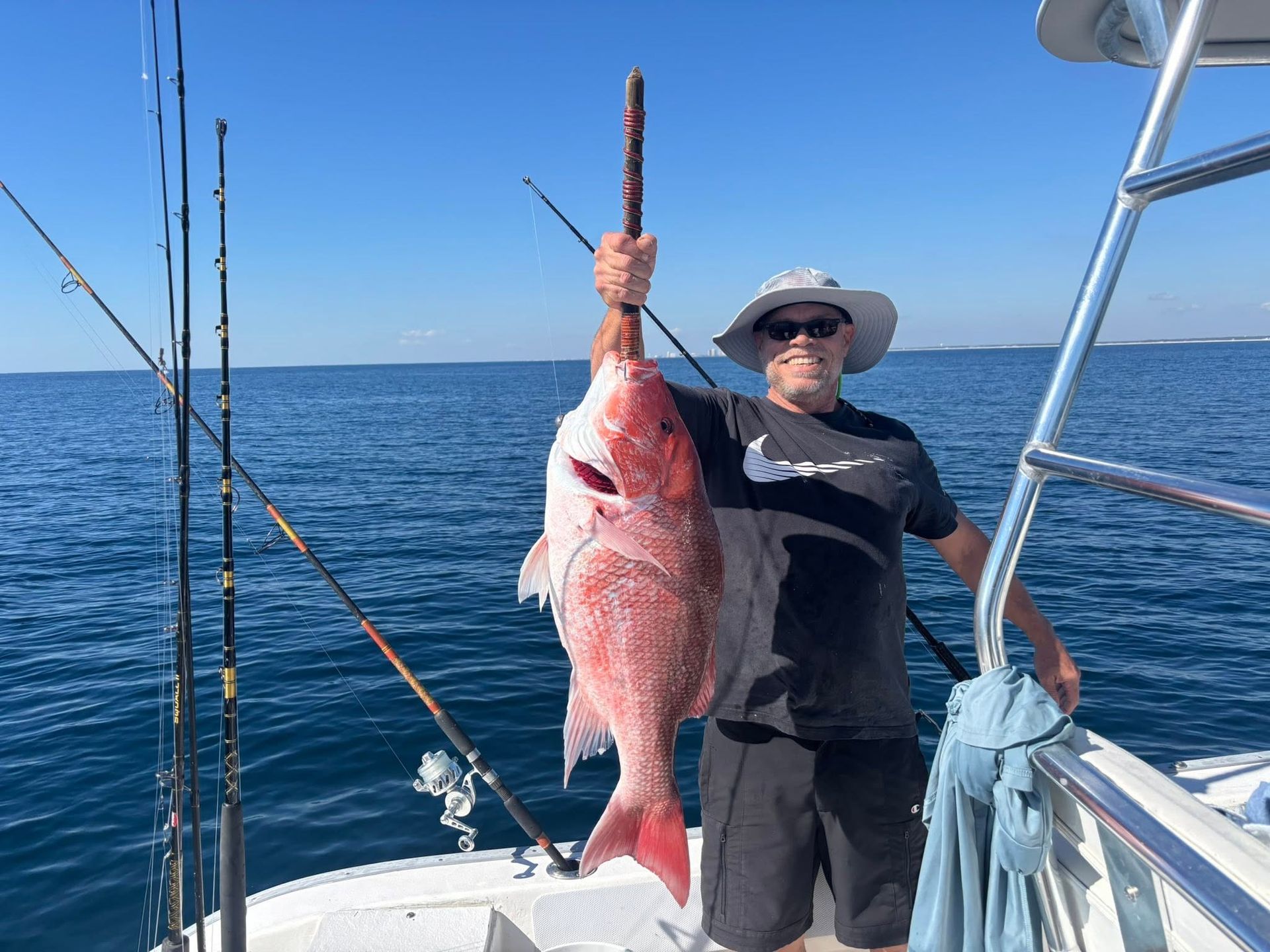 Man on a boat holding a large red fish by the tail on a sunny ocean day