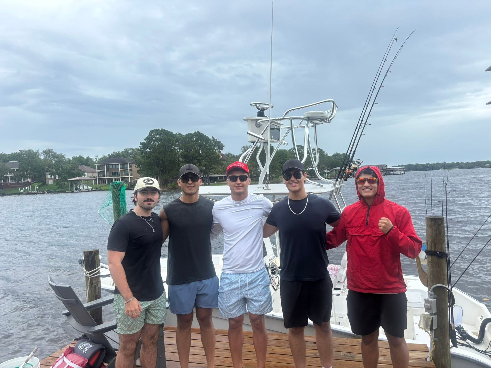 Five people posing on a boat dock with a fishing boat and water in the background