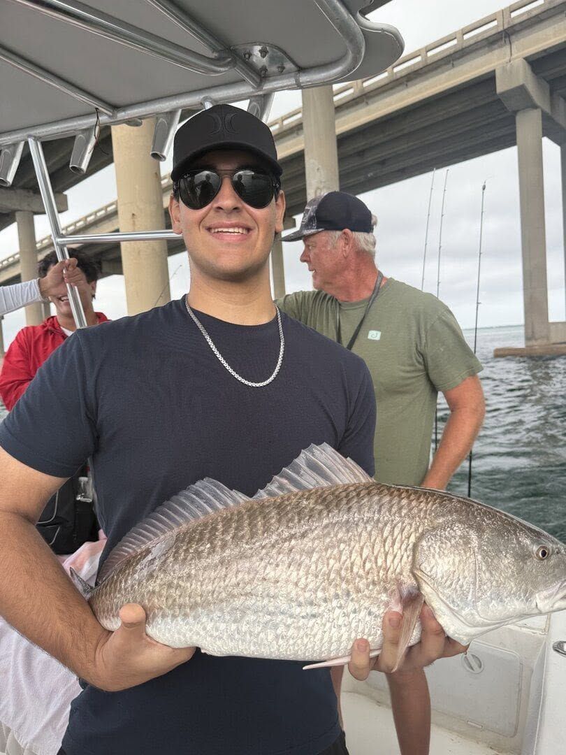 Smiling angler on a boat holding a large fish, with another man in the background.