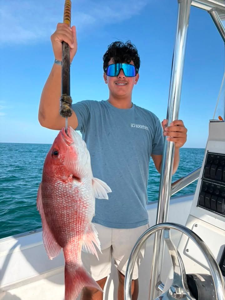 Man on a boat holding a large red fish on a rope, with the ocean in the background.