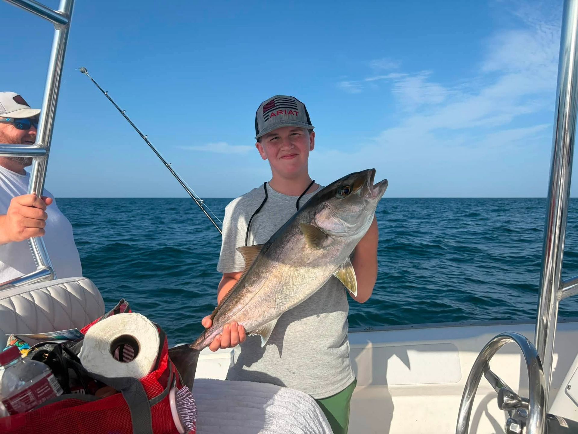Person holding a large fish on a boat with the ocean and blue sky in the background