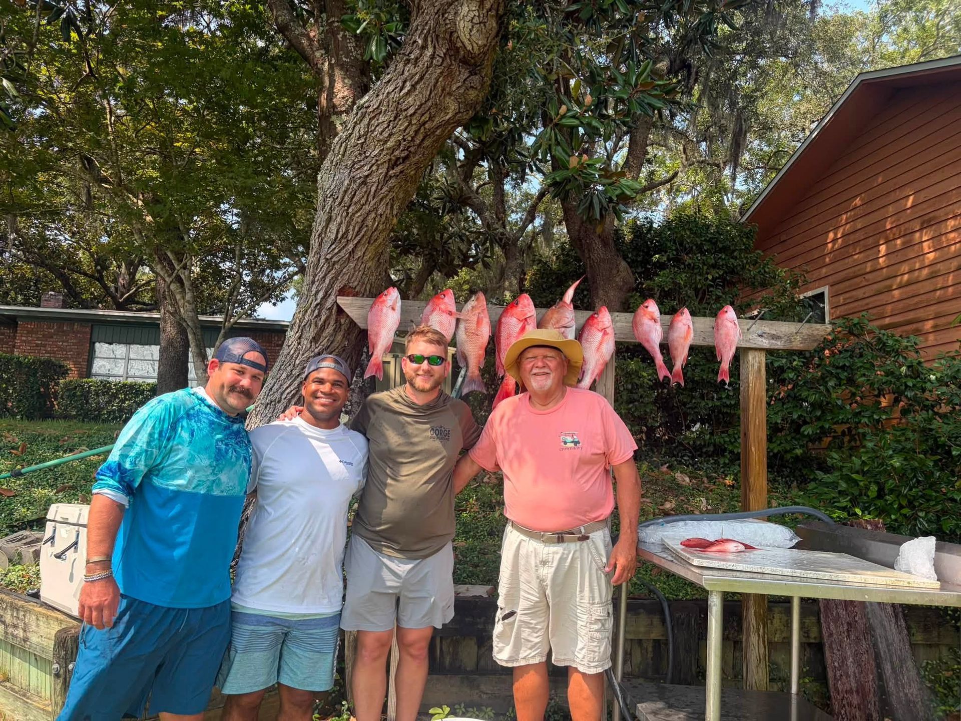 Four people posing by hanging fish outdoors at a backyard cookout