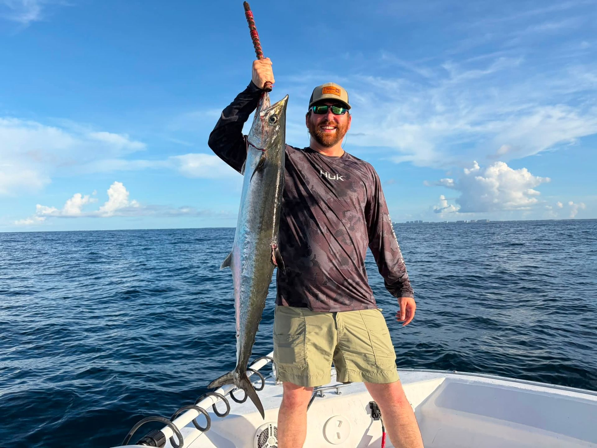 Person on a boat holding up a large fish on a sunny ocean.