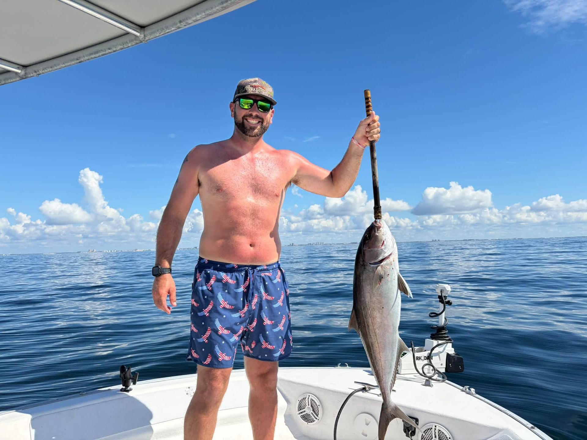 Smiling angler on a boat holding a large fish over calm blue ocean