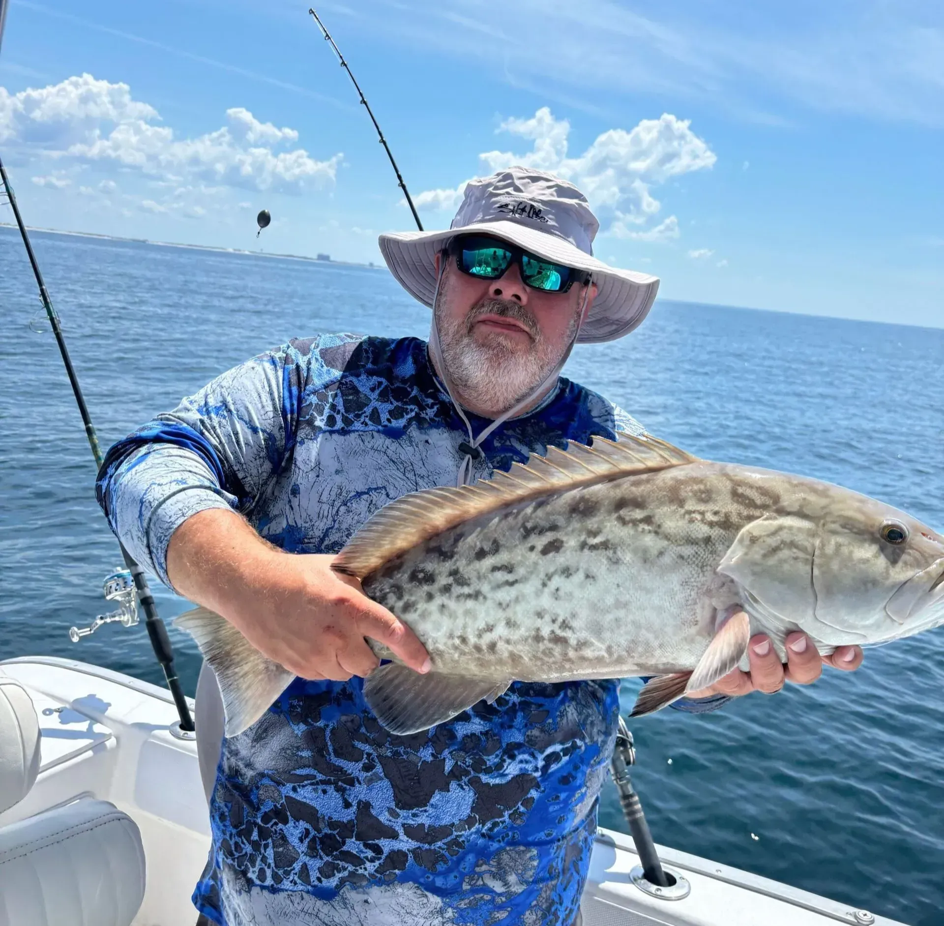 Angler on a boat holding a large spotted fish on a sunny ocean day