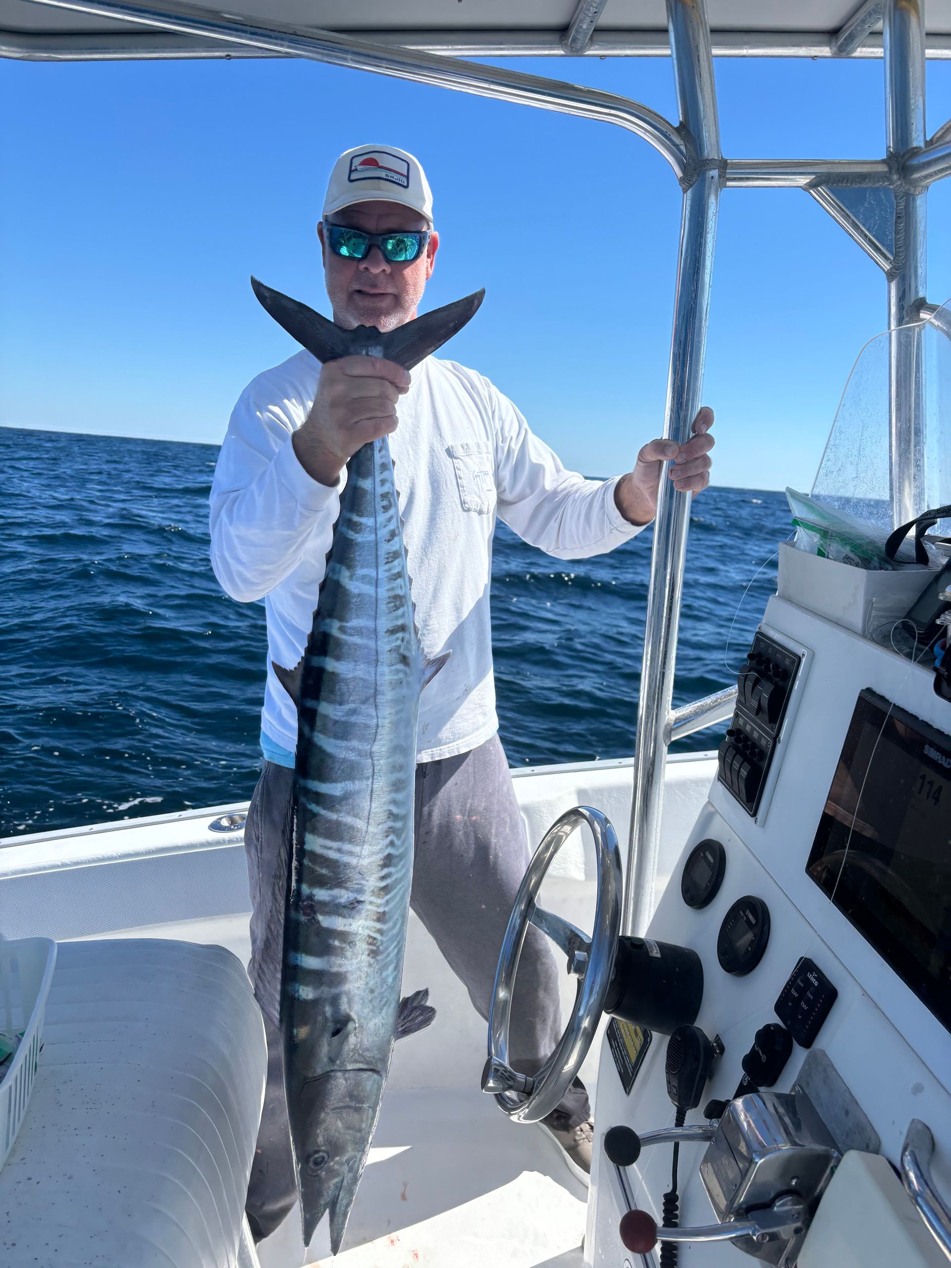 Person on a boat holding a long striped fish against a blue ocean backdrop