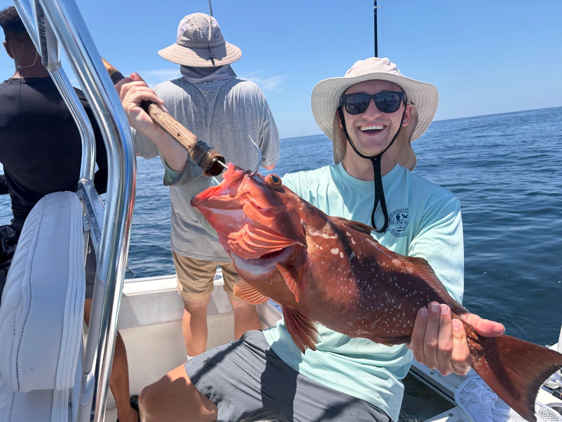 Smiling person on a boat holding a large red fish, with the ocean in the background.