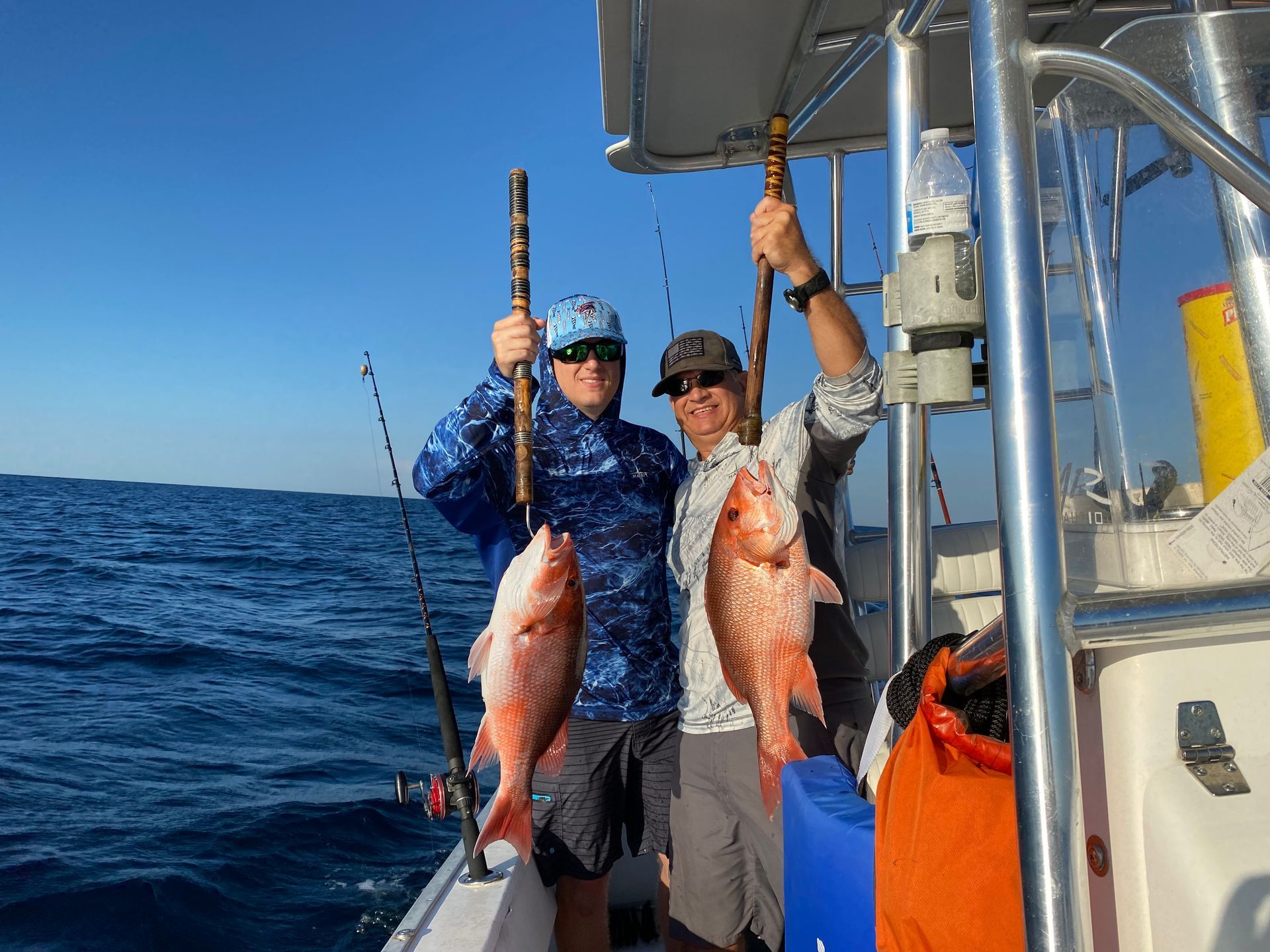 Two anglers on a boat holding up large fish on a sunny ocean trip