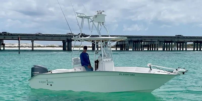 White fishing boat on turquoise water near a bridge, with a person at the helm