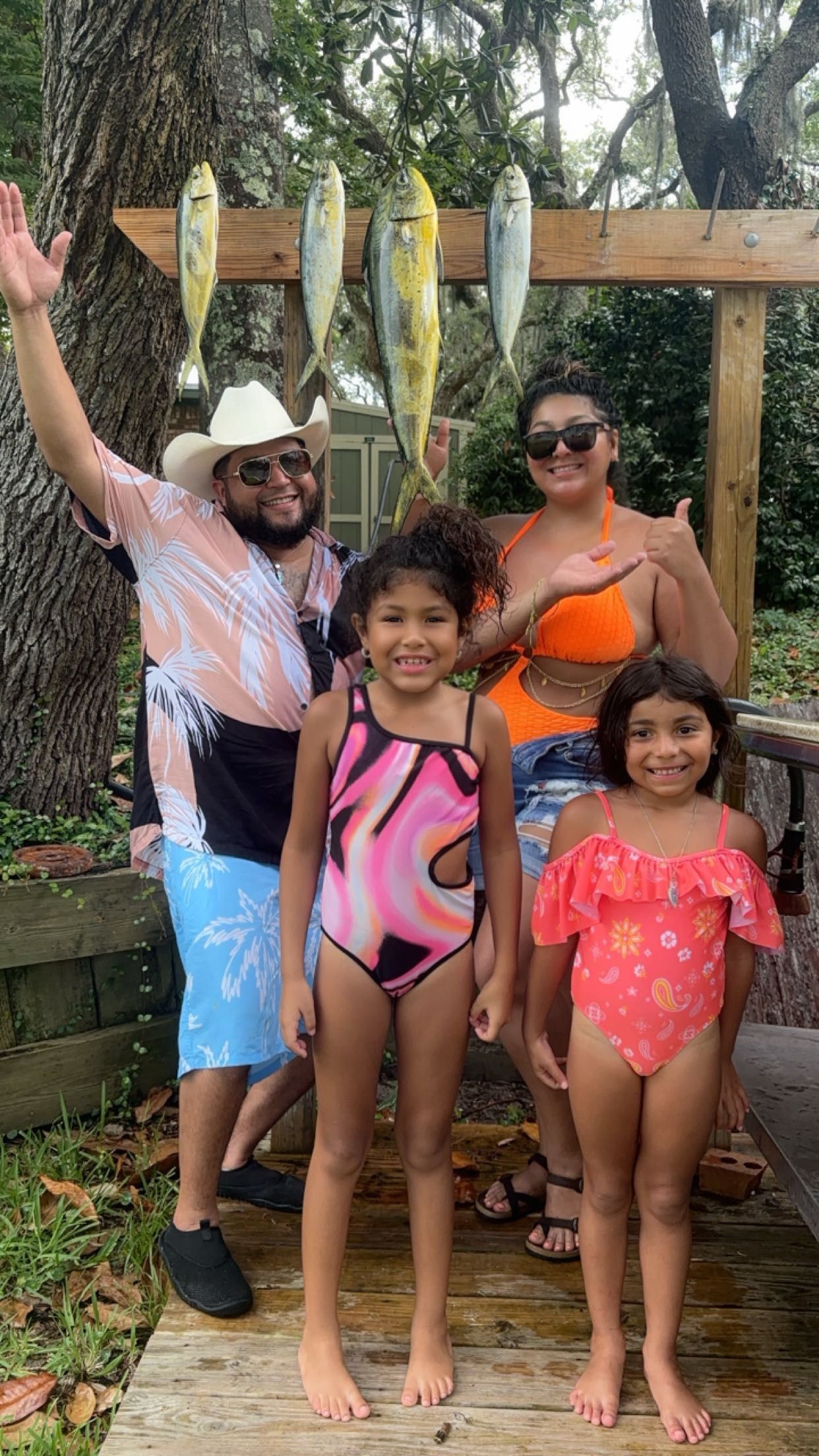 Family posing outdoors by a wooden pergola, with two children in front and adults smiling behind.