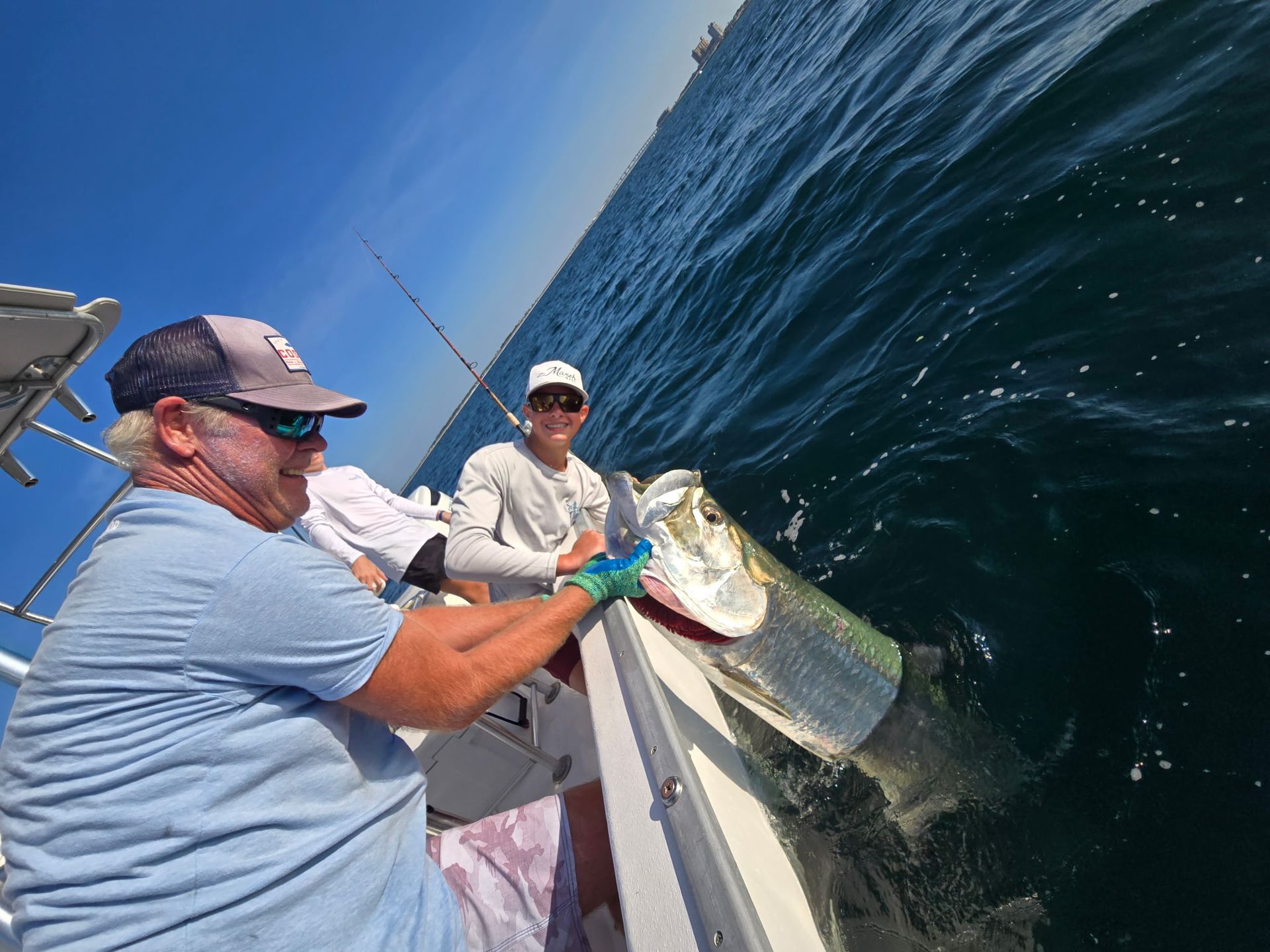 Two anglers on a boat reel in a large fish beside deep blue water.