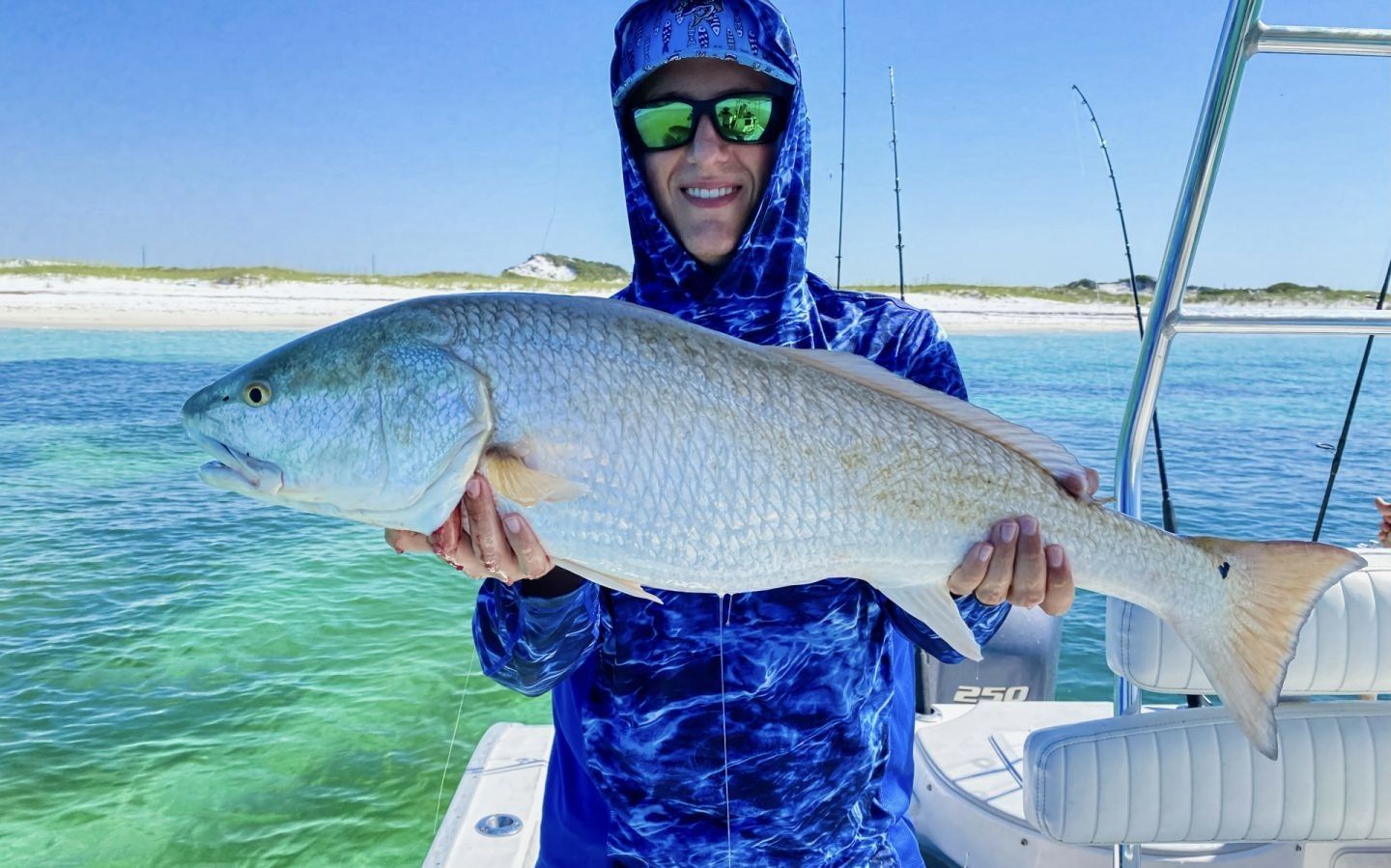 Person in blue sun gear holding a large fish on a boat in clear blue water