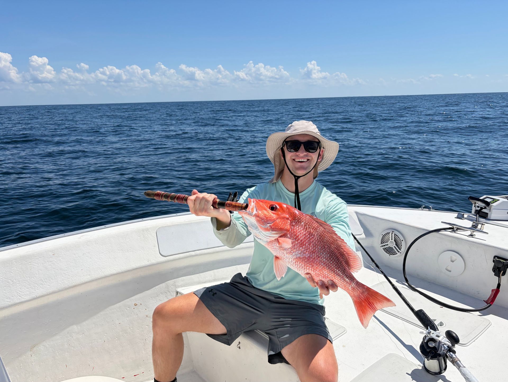 Person on a boat holding a large red fish on the open ocean under a blue sky.