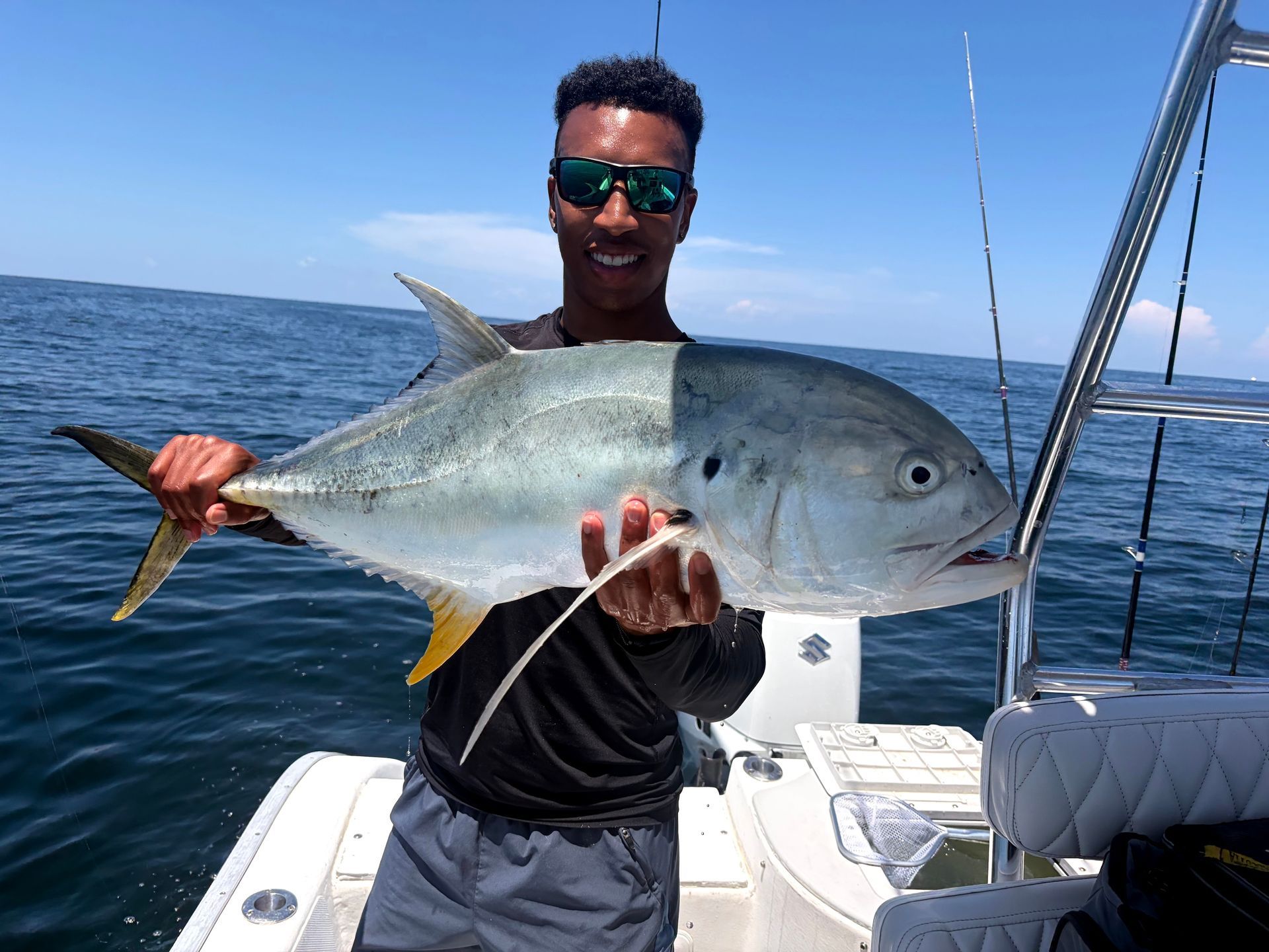 Man on a boat holding a large silver fish on the open ocean under a clear sky