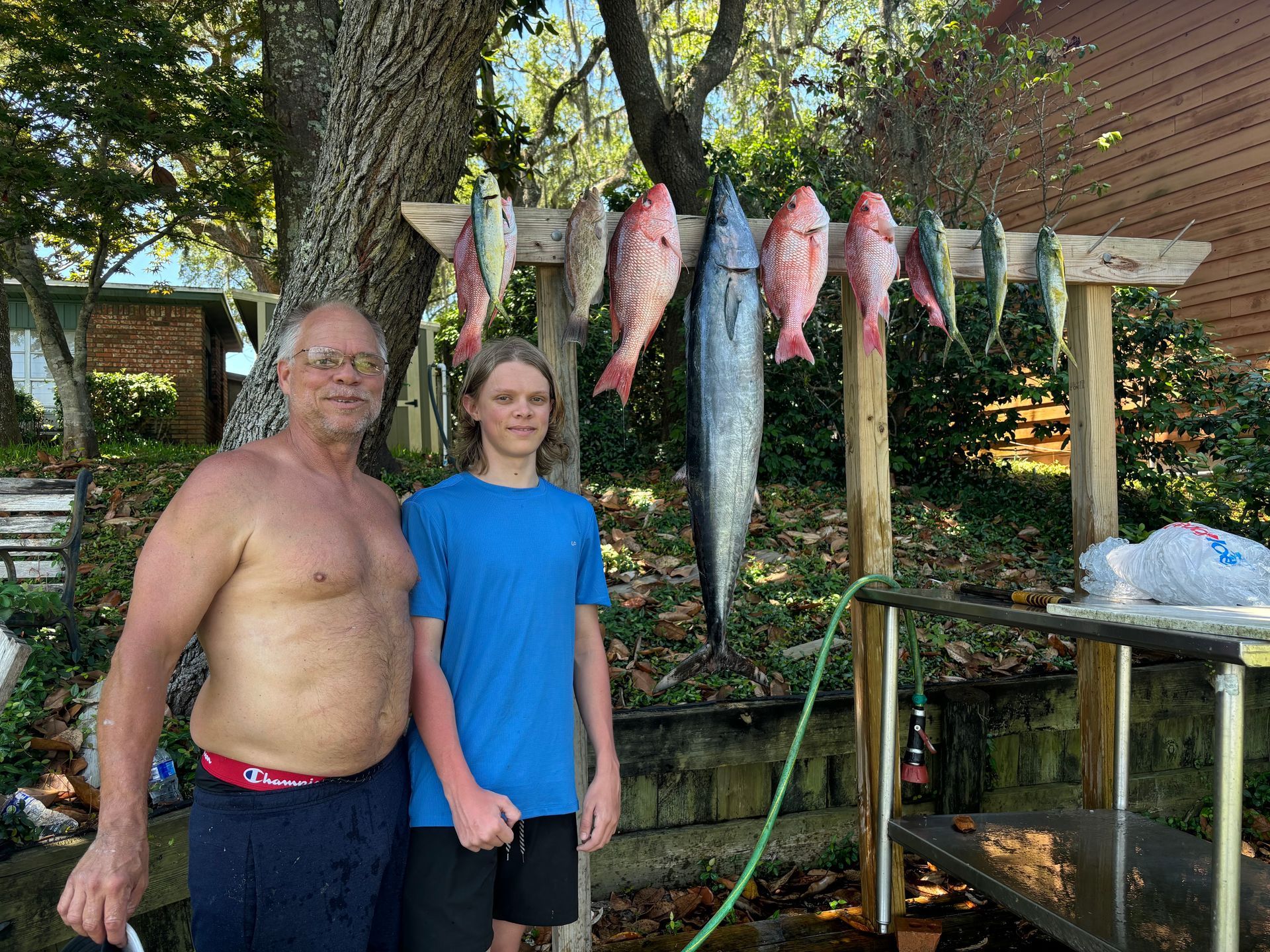 Two people stand by a tree with several fish hanging from a line outdoors.