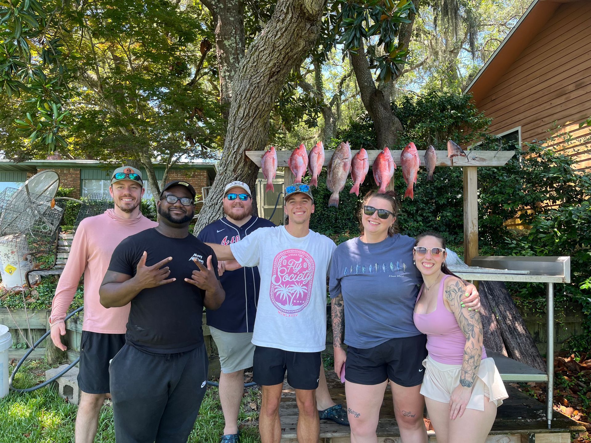 Five people posing outdoors beside a fish rack and cabin, smiling in casual clothes.