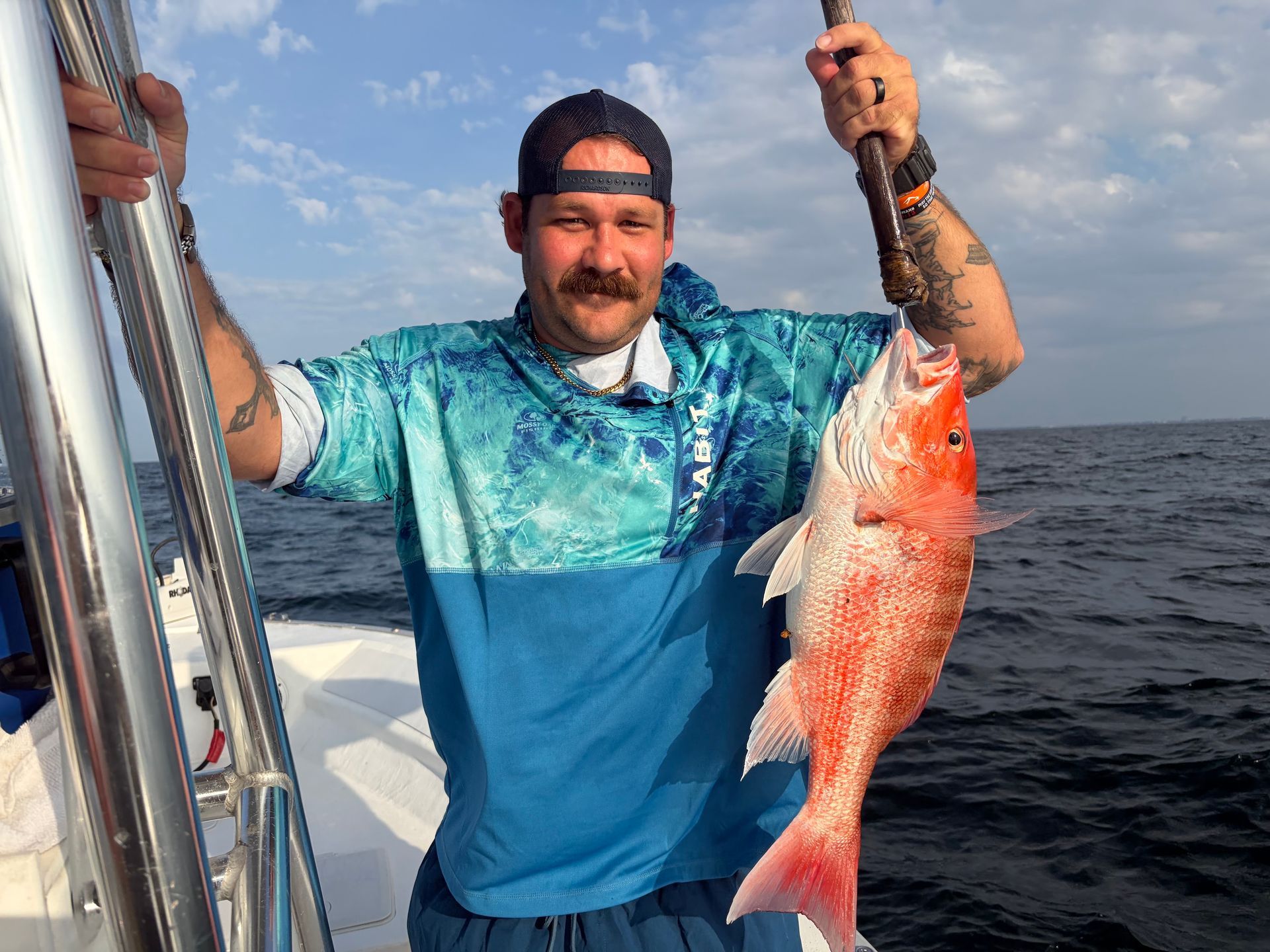 Man holding a large red fish on a boat at sea, wearing a blue shirt and cap.
