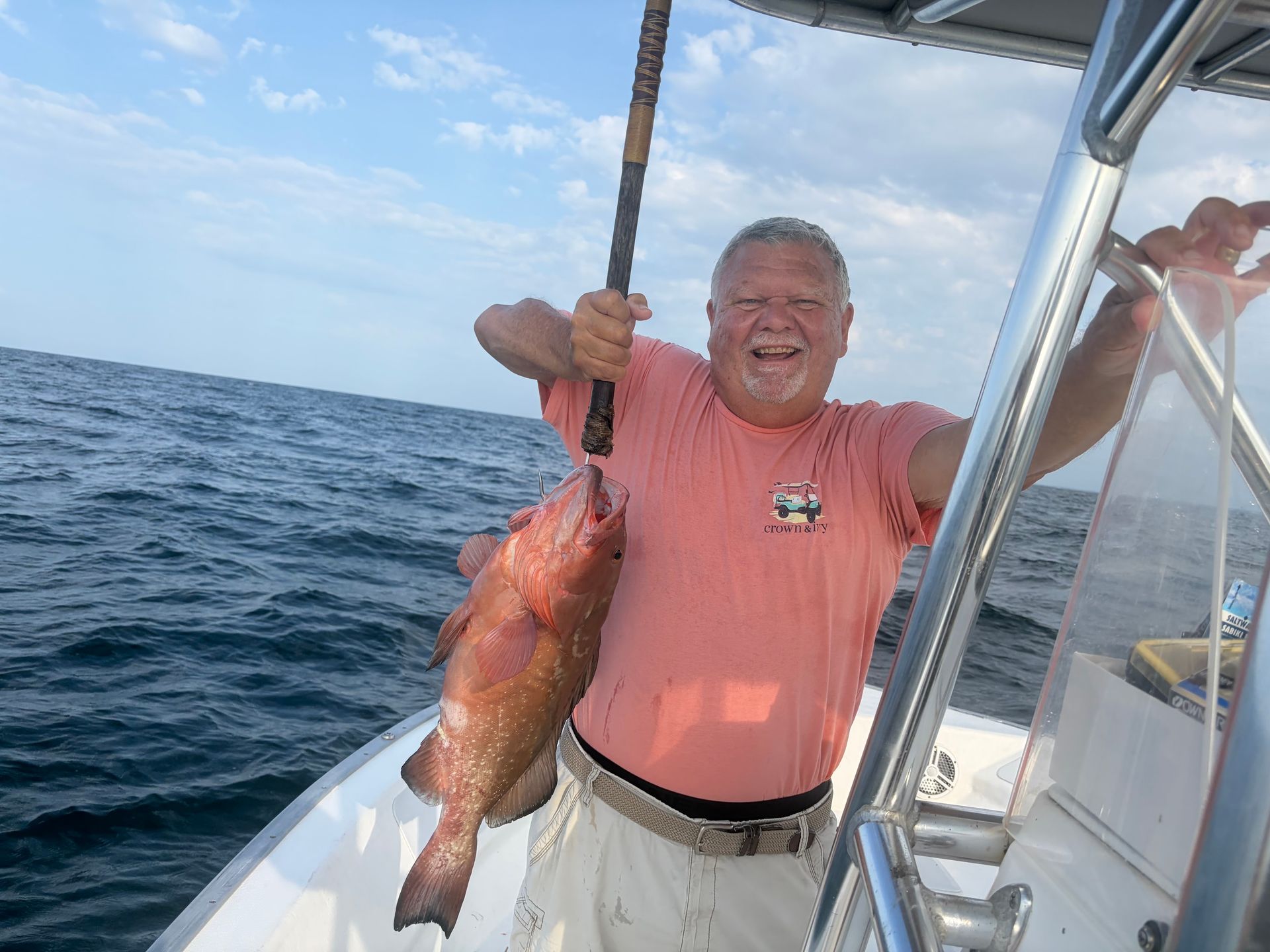Man on a boat holding a large fish, smiling on the ocean under a blue sky