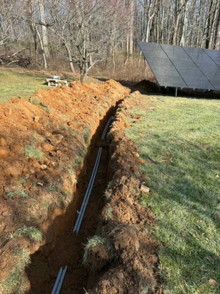 Trenched dirt beside a grassy yard with black solar panels in the background.