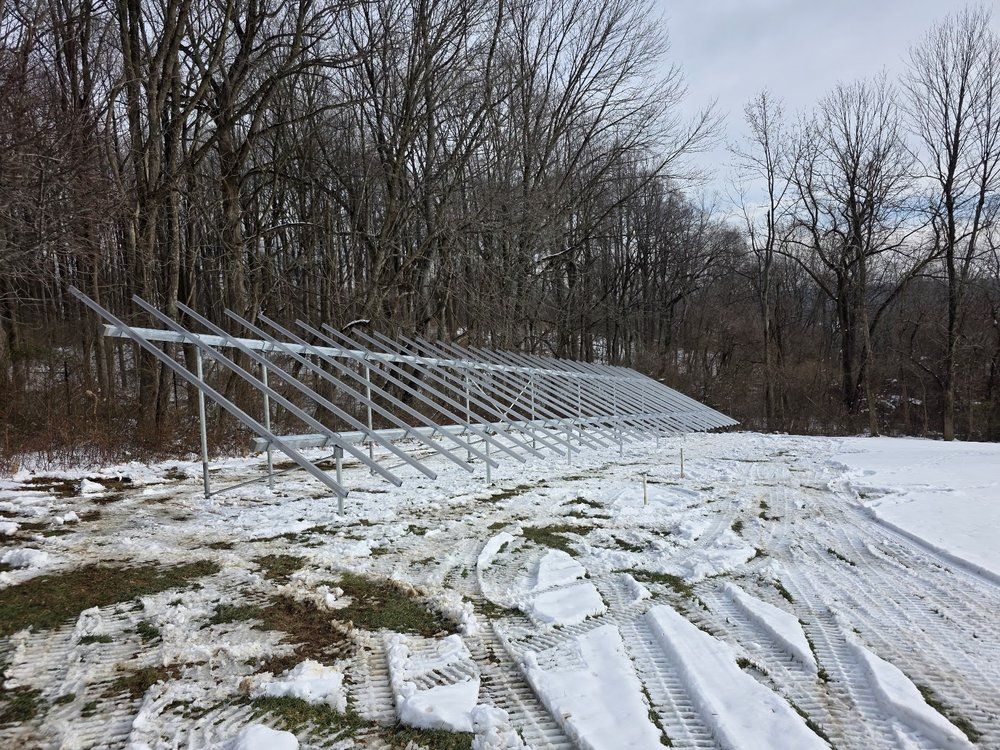Snow-covered solar panel array beside a wooded area on a winter day