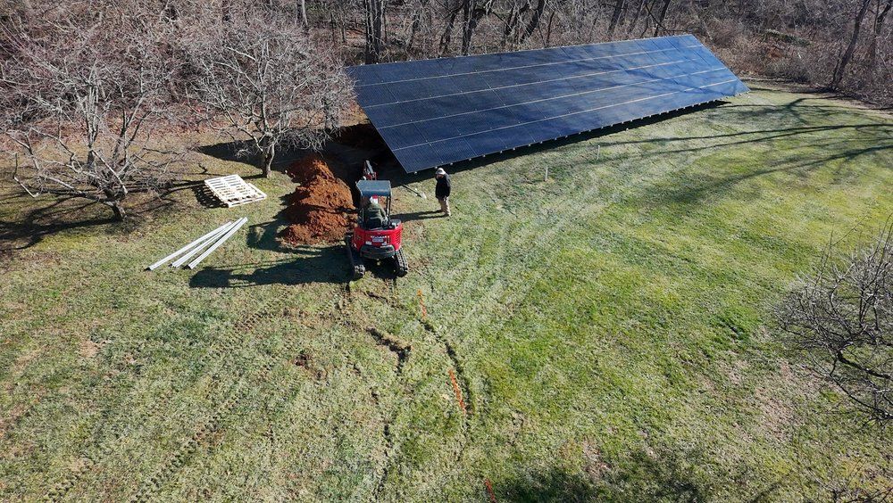 Workers installing a large blue solar panel on a grassy hillside beside trees