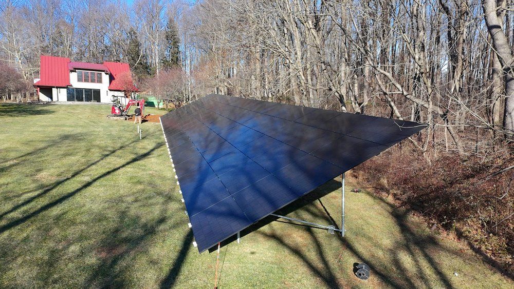 Black tarp shelter stretched over a frame in a grassy yard near a red barn and leafless trees.