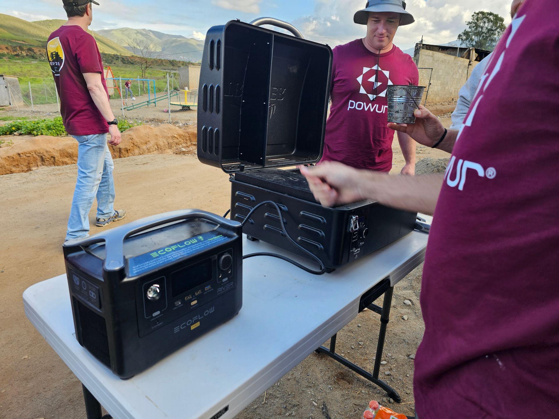 People setting up black portable power stations on a folding table outdoors.