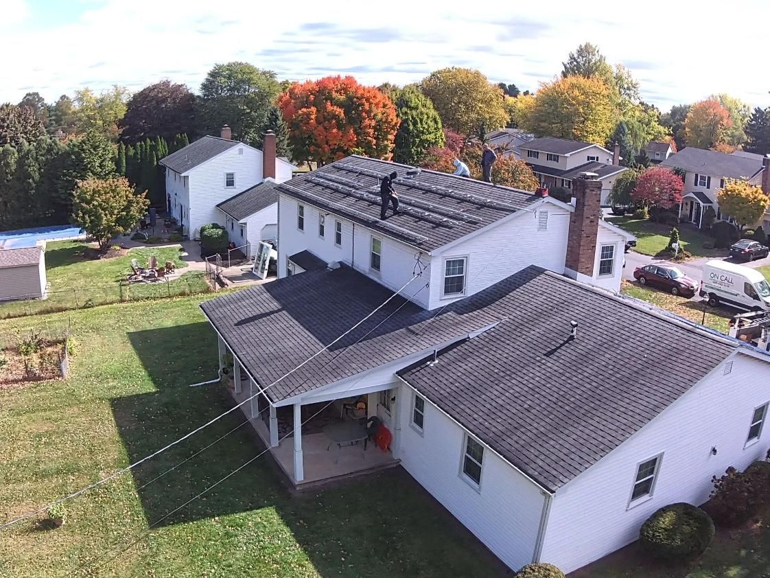 Aerial view of a white house with a dark gray roof in a suburban neighborhood with colorful trees.