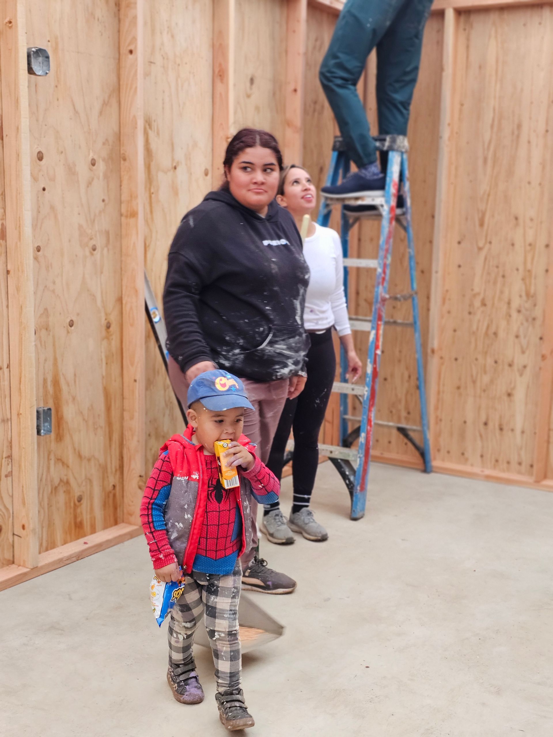 Three people and a child in a room with wooden walls, one on a ladder and two standing nearby.