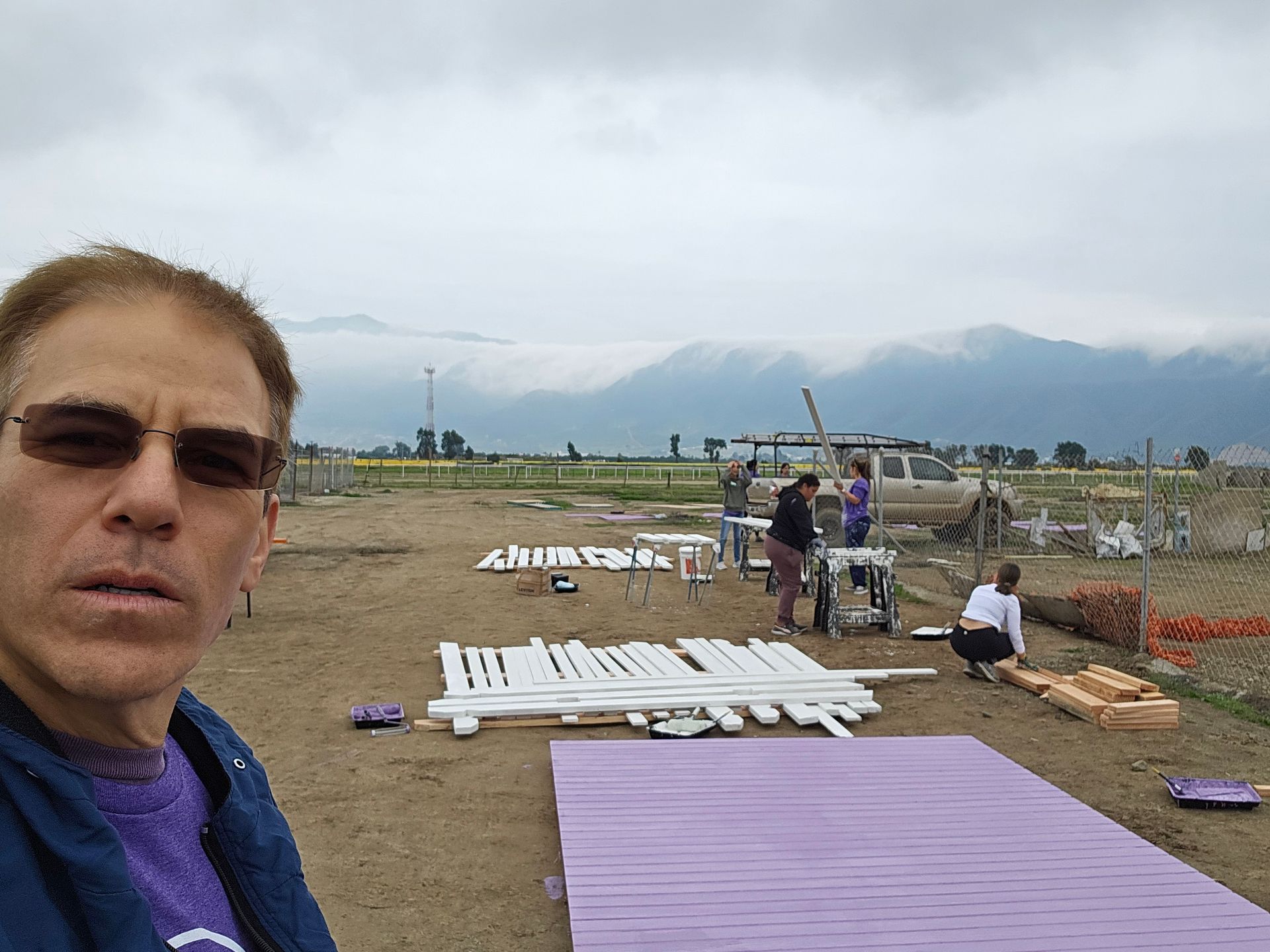 Selfie at a construction site with purple and white panels laid out on the ground, mountains in the background
