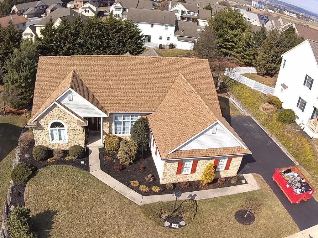 Aerial view of a suburban house with brown roof, stone facade, and red shutters. 