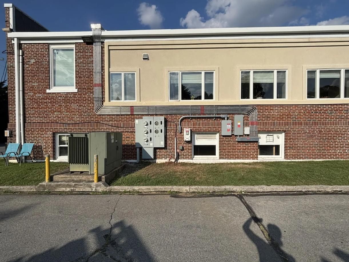 Brick and tan building exterior with several windows, electrical boxes, and air conditioning unit.
