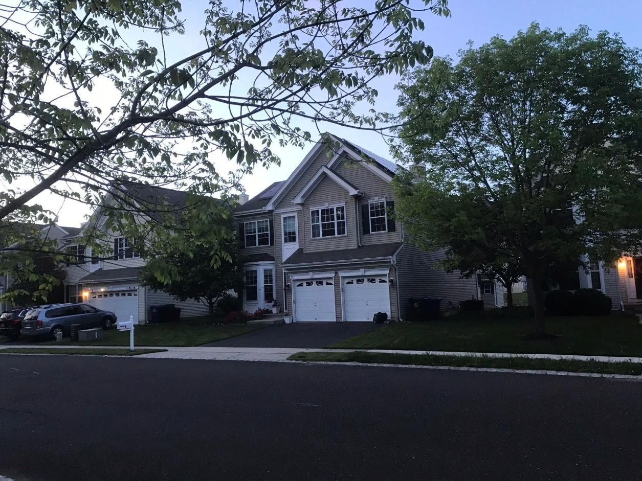 Two-story house with a three-car garage, fronted by a dark driveway and lawn, shaded by trees.