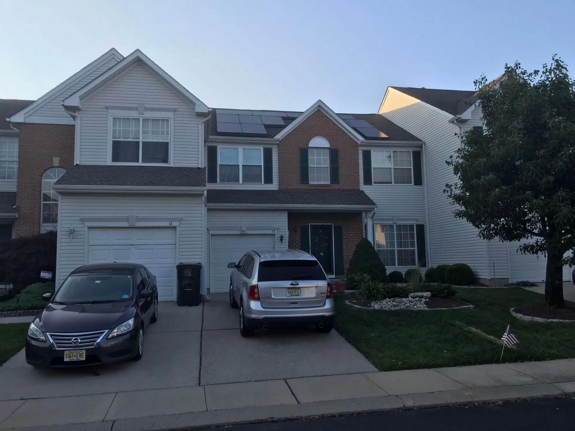 Two-story house with cars in driveway, solar panels on the roof, and a small front yard.