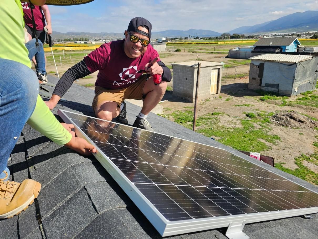 Two people installing a solar panel on a roof with a rural landscape in the background.