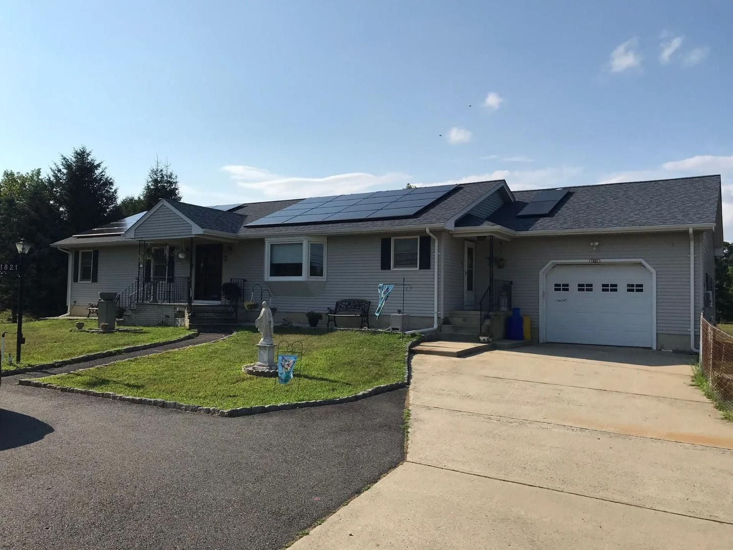 Gray house with solar panels on the roof, a driveway, and a lawn under a blue sky.